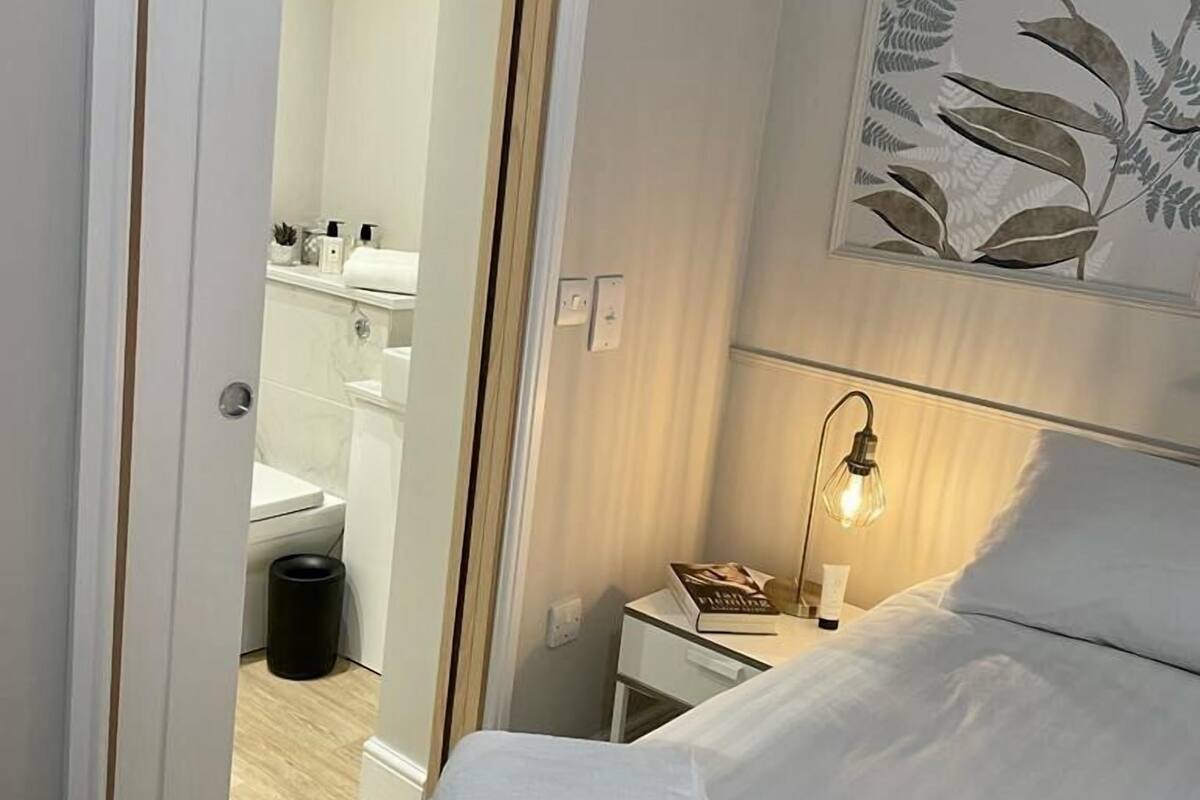 A hotel room with a bed, a nightstand, a lamp, a painting, and a bathroom visible through an open door.