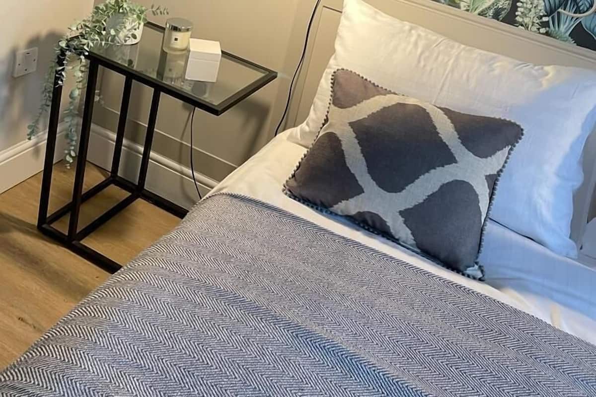 A bedroom with a floral wallpaper, a bedside table with a lamp, and a bed with patterned bedding.