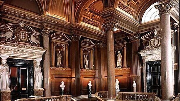 Ein prunkvolles Interieur mit monumentalen Säulen, einer zentralen Treppe und klassischen Statuen.