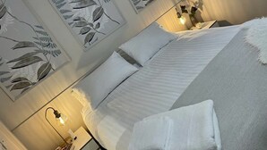 Ein ordentlich bezogenes Bett mit weißen Leinen, eine Nachttischlampe und ein dekoratives Wandbild darüber.