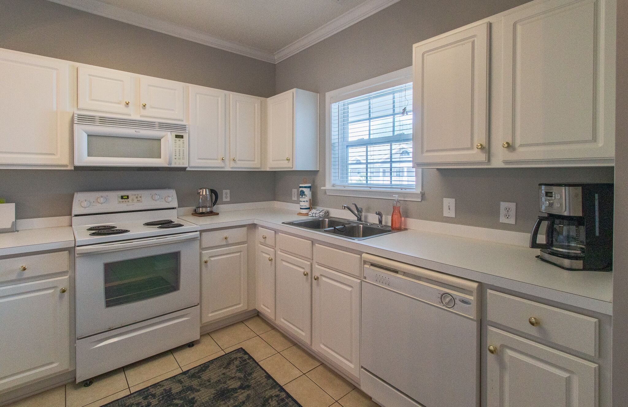 A kitchen with white cabinets, a microwave, a stove, a sink, and a window with blinds.