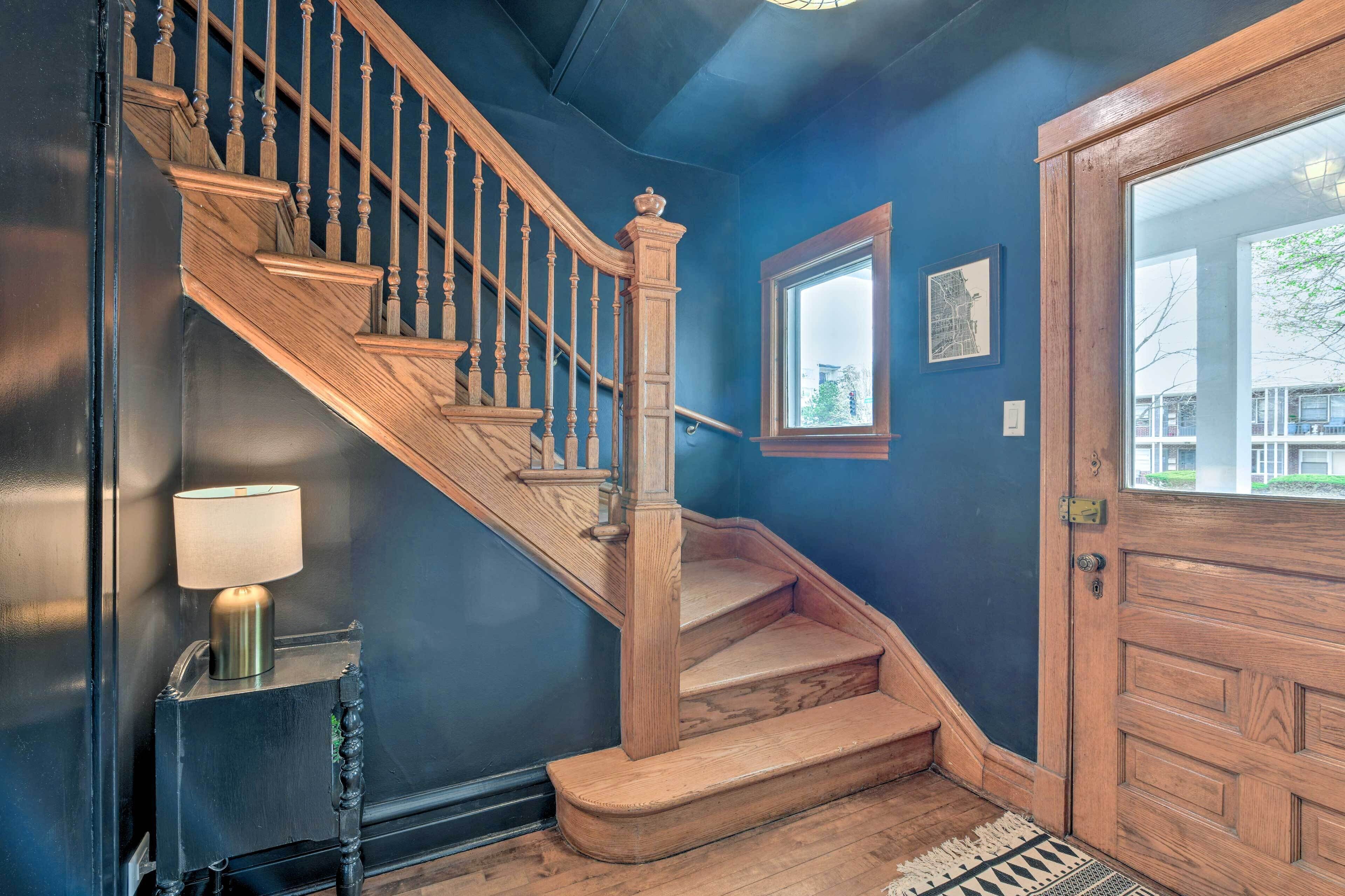 Un escalier en bois avec une lampe sur la plateforme, une porte avec une fenêtre et un tapis sur le sol.
