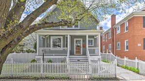 A two-story house with a porch, a white picket fence, and a brick building adjacent to it. - Spacious Oak Park Home, 11 Mi to Downtown Chicago! (Oak Park)