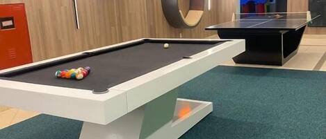 Uma mesa de bilhar com moldura branca e chão coberto por carpete verde.