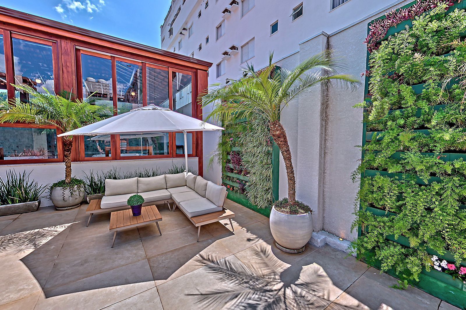 Un espacio al aire libre con sillones, una mesa y una sombrilla, rodeado de macetas con plantas y un jardín vertical.