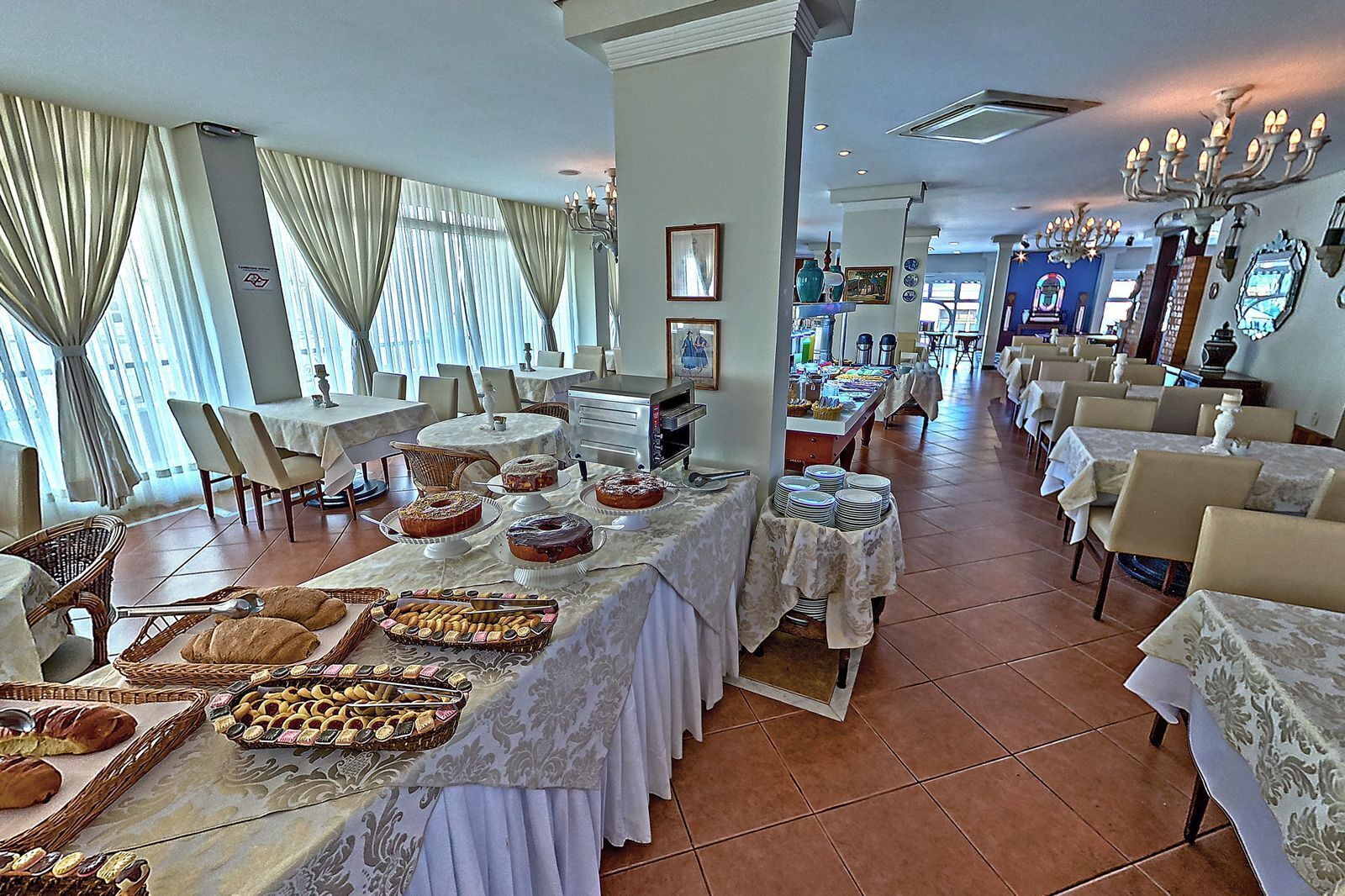 A dining area with tables set for breakfast, featuring pastries and bread.
