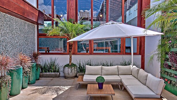Un patio moderno al aire libre con un sofá modular, una mesa de madera y una sombrilla grande.