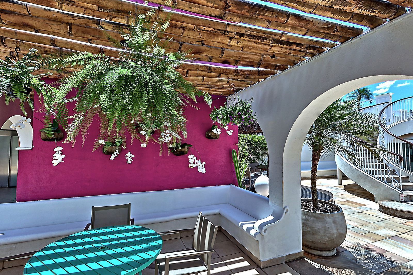 A covered outdoor seating area with a pink wall, hanging plants, and a staircase leading to an upper level.