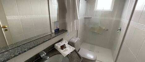 Un baño moderno con encimera de granito, lavamanos, inodoro y ducha con mampara de vidrio.