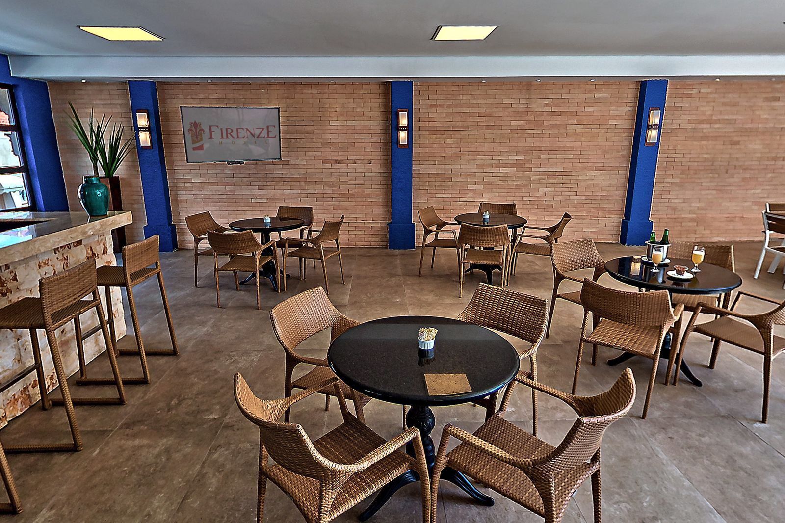 Een hotel lobby met rieten meubels, een bar en een bord met de tekst 'FIRENZE HOTEL'.