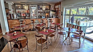 A restaurant with multiple wooden tables and chairs, a brick wall, and shelves with various items.