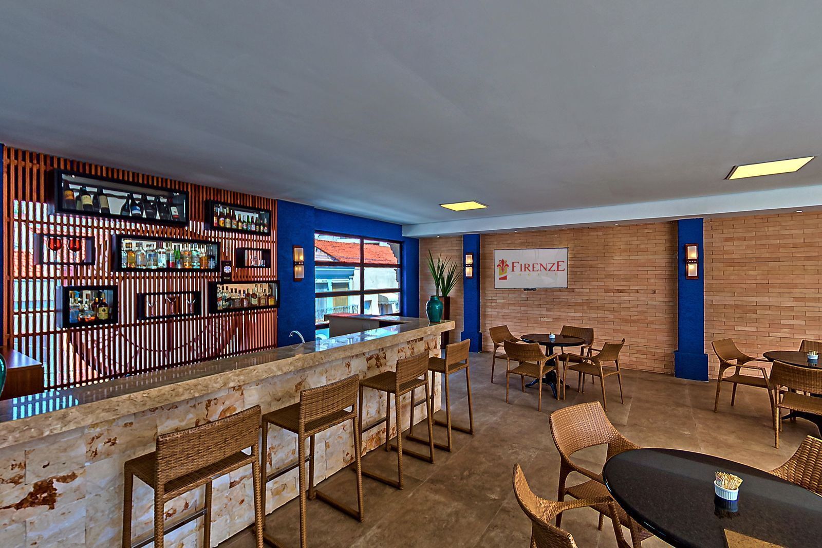 A bar area with a wooden counter and wicker chairs, a sign reading "FIRENZE", and a view through a large window.