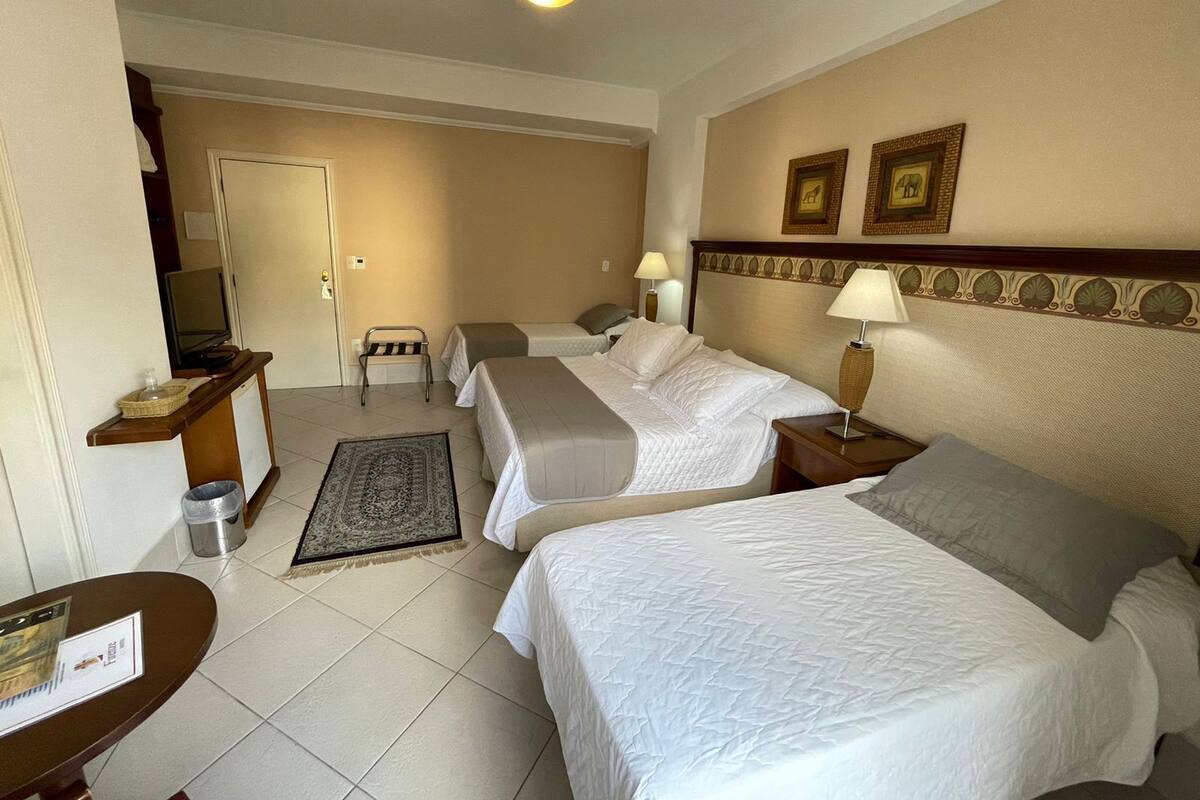 A hotel room with two beds, a desk, a chair, a television, and a ceiling fan.