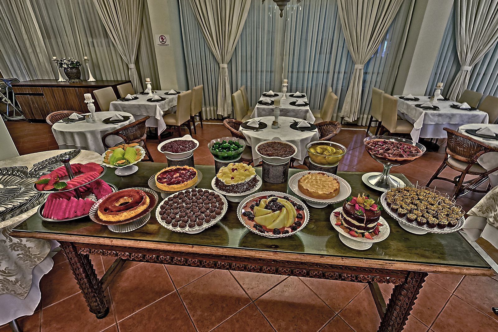 Un espace repas avec plusieurs tables dressées pour un buffet, proposant une variété de desserts et de plats.