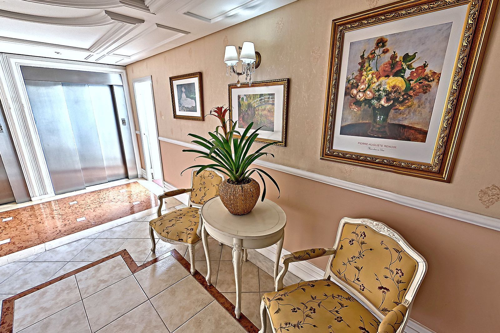 A lobby with a round table, floral-patterned chairs, a potted plant, and framed artwork on the walls.