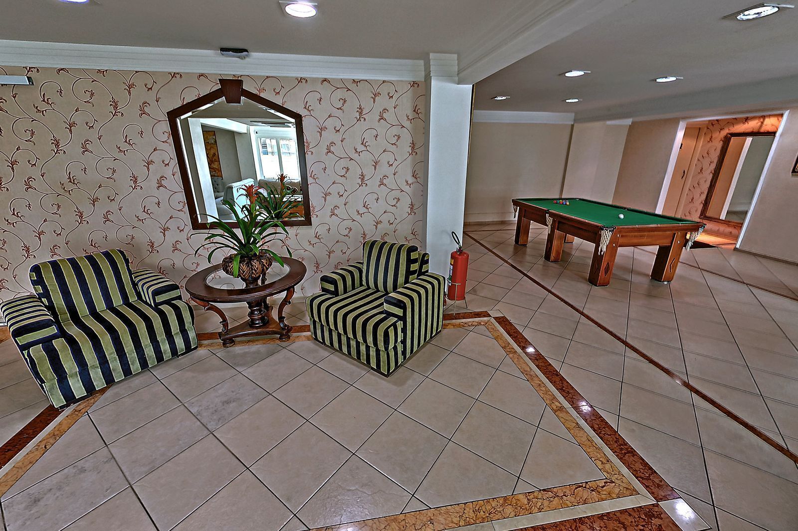 A room with striped sofas, a pool table, and a mirror on the wall.