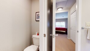 Ein schmaler Flur führt zu einem Schlafzimmer mit Bett, Fenster und einem Badezimmer mit Toilette und Waschbecken.
