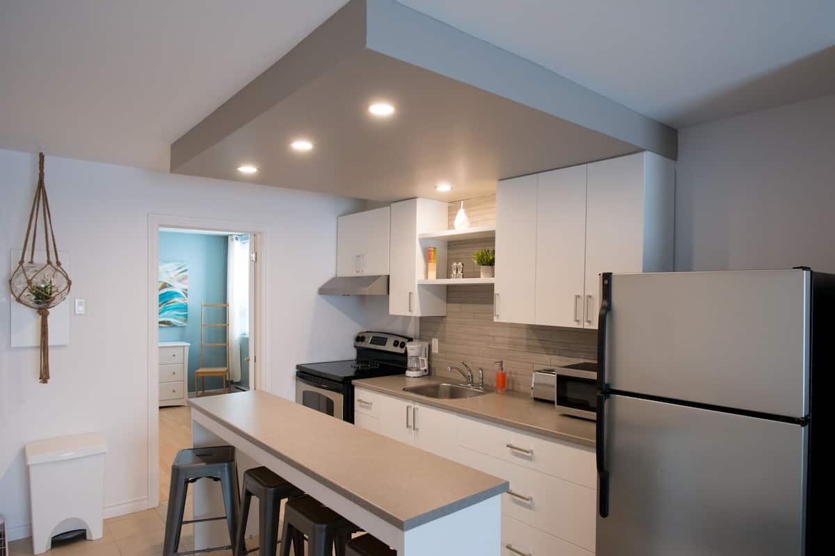 A modern kitchen with white cabinets, a stainless steel refrigerator, and a central island with bar stools.