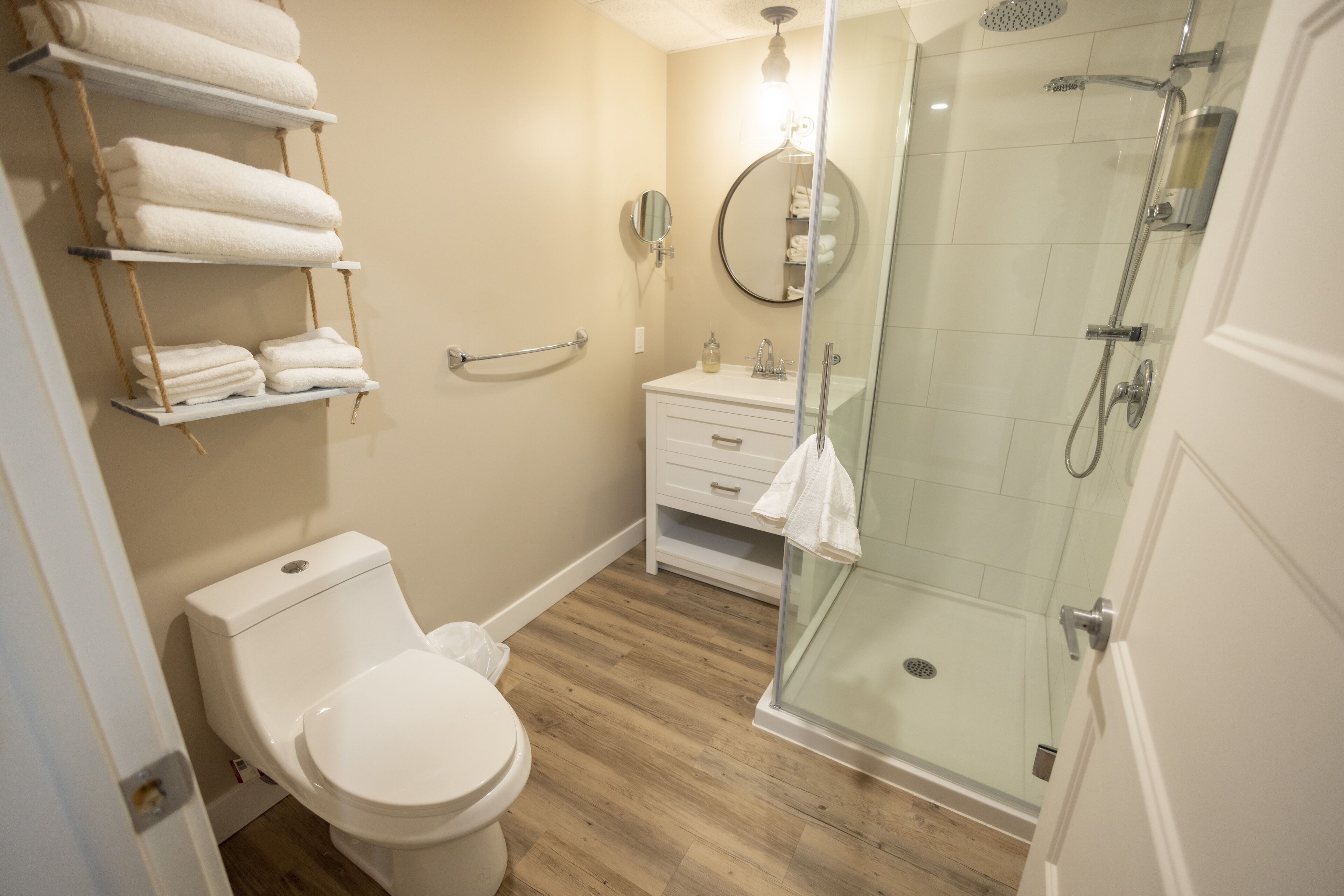 A bathroom with a toilet, a sink, a glass-enclosed shower, and a towel rack with folded towels.