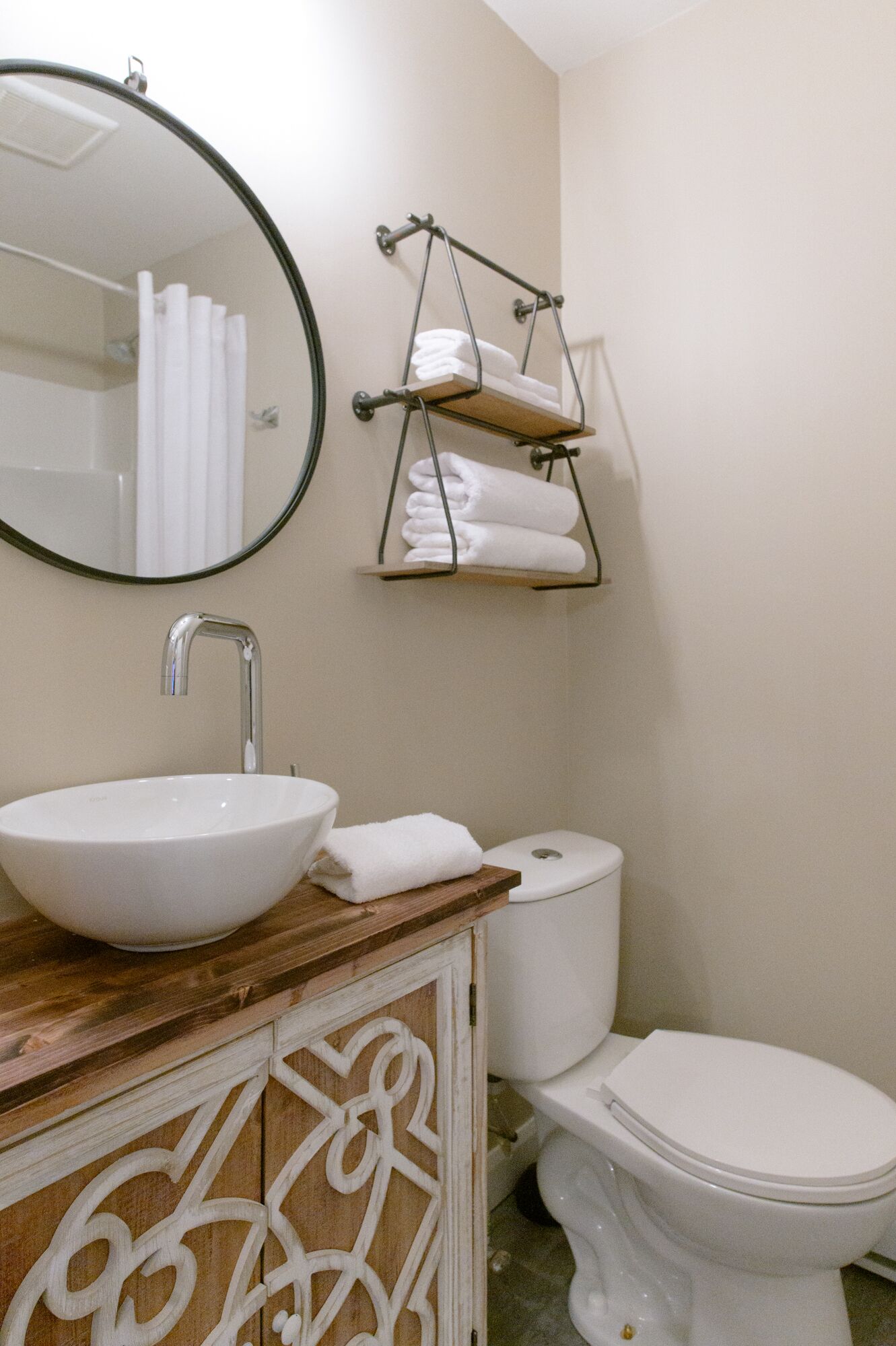 Un bagno con uno specchio tondo, un lavandino bianco, un water e un portasciugamani.
