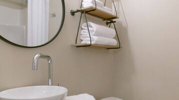 Un bagno con uno specchio tondo, un lavandino bianco, un water e un portasciugamani.