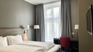 Une chambre d’hôtel avec un grand lit, deux lampes de chevet, un bureau avec une chaise et une grande fenêtre avec des rideaux.