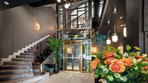 Un hall d’hôtel moderne avec un escalier en marbre, un ascenseur en verre et un grand arrangement floral.