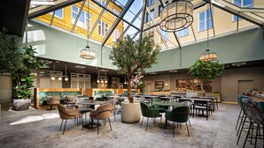 Un vaste espace intérieur aménagé avec différents coins salon, un arbre central et un coin cuisine à l’arrière-plan.