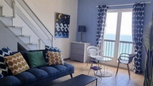 A living room with a blue sofa, a coffee table, a white dresser, and a staircase. - Large apartment with sea/village view 200m from the beach (Saint-Florent)
