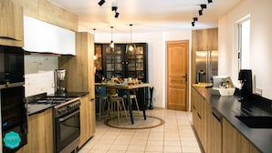 Una cuina moderna amb armaris de fusta, un forn encastrat, una zona de menjador amb tamborets i una finestra gran.