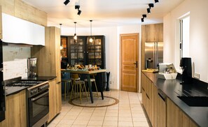 Une cuisine moderne avec des meubles en bois, un four encastré, un coin repas avec des tabourets et une grande fenêtre.