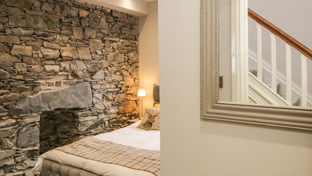 Un dormitorio con pared de piedra, una cama con colcha a cuadros y un espejo con marco de madera.