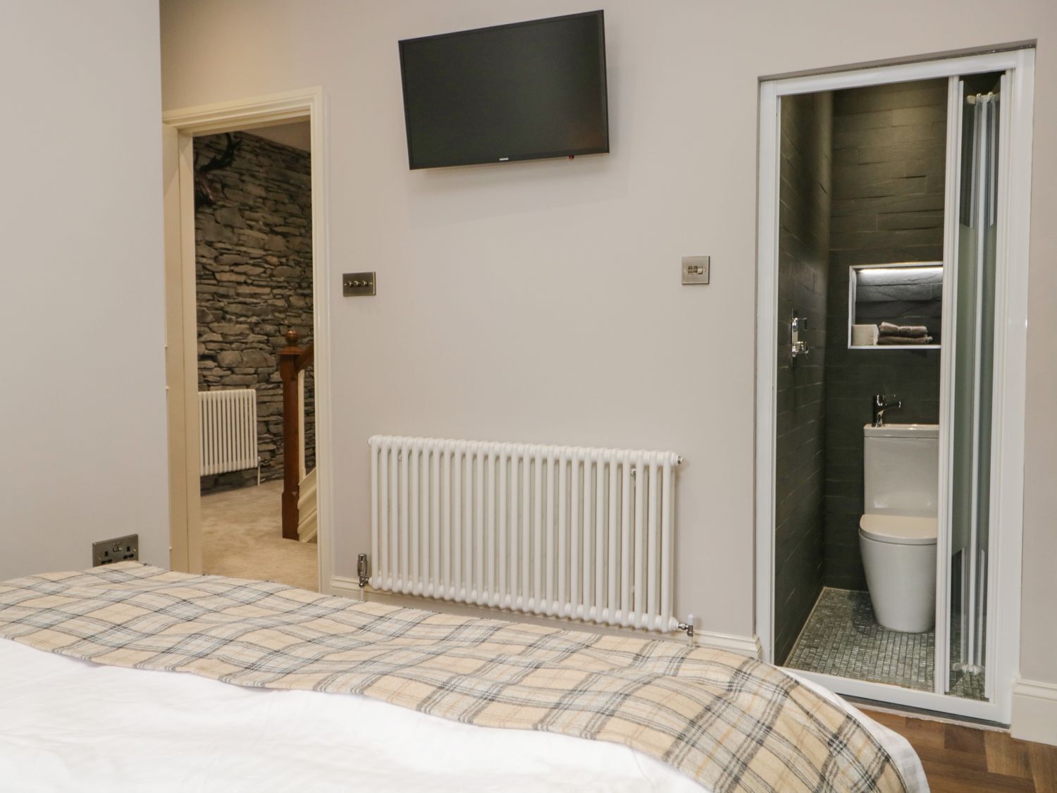 A bedroom with a bed, a television, a bathroom with a toilet and sink, and a stone wall.