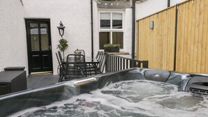 Un jacuzzi en un patio con una mesa, sillas, una puerta y una cerca de madera.
