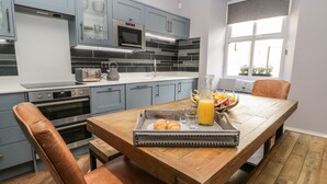 Una cocina moderna con armarios grises, una mesa de comedor de madera y una mesa para el desayuno con croissants y jugo de naranja.