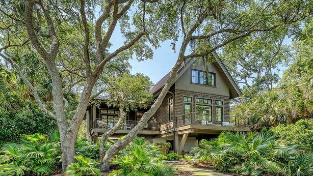 A two-story house with a large deck, surrounded by lush greenery and trees. - New Build in desirable Ocean Park community (Kiawah Island)