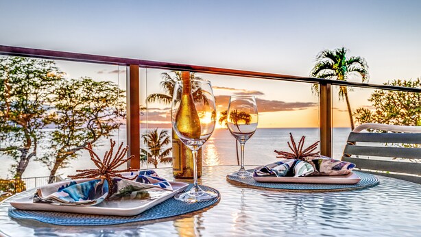 A table set for two with wine glasses, plates, and a decorative centerpiece, overlooking a sunset view.