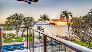 A poolside view with a sunset over the ocean, palm trees, and outdoor seating.