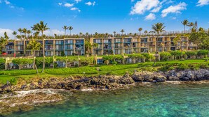 A coastal hotel with multiple balconies, lush greenery, and clear waters.