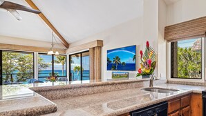 A kitchen with granite countertops, a dishwasher, wooden cabinets, and a view of the ocean.