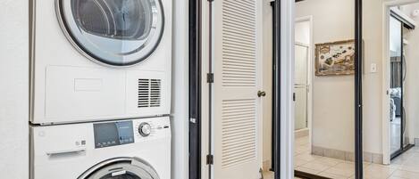 A laundry room with stacked washing machines and dryers, a door leading to another room, and a tiled floor.