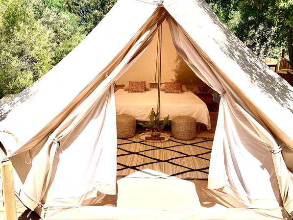 A tent with a bed, pillows, and a woven mat inside.