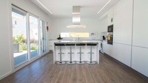A modern kitchen with a central island, bar stools, a built-in oven, and a large window. - Dalma- Villa da Ourada (Albufeira)