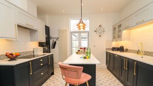A modern kitchen with black cabinets, a white countertop, and a central island with a pink chair. - Seaside House (Weymouth)