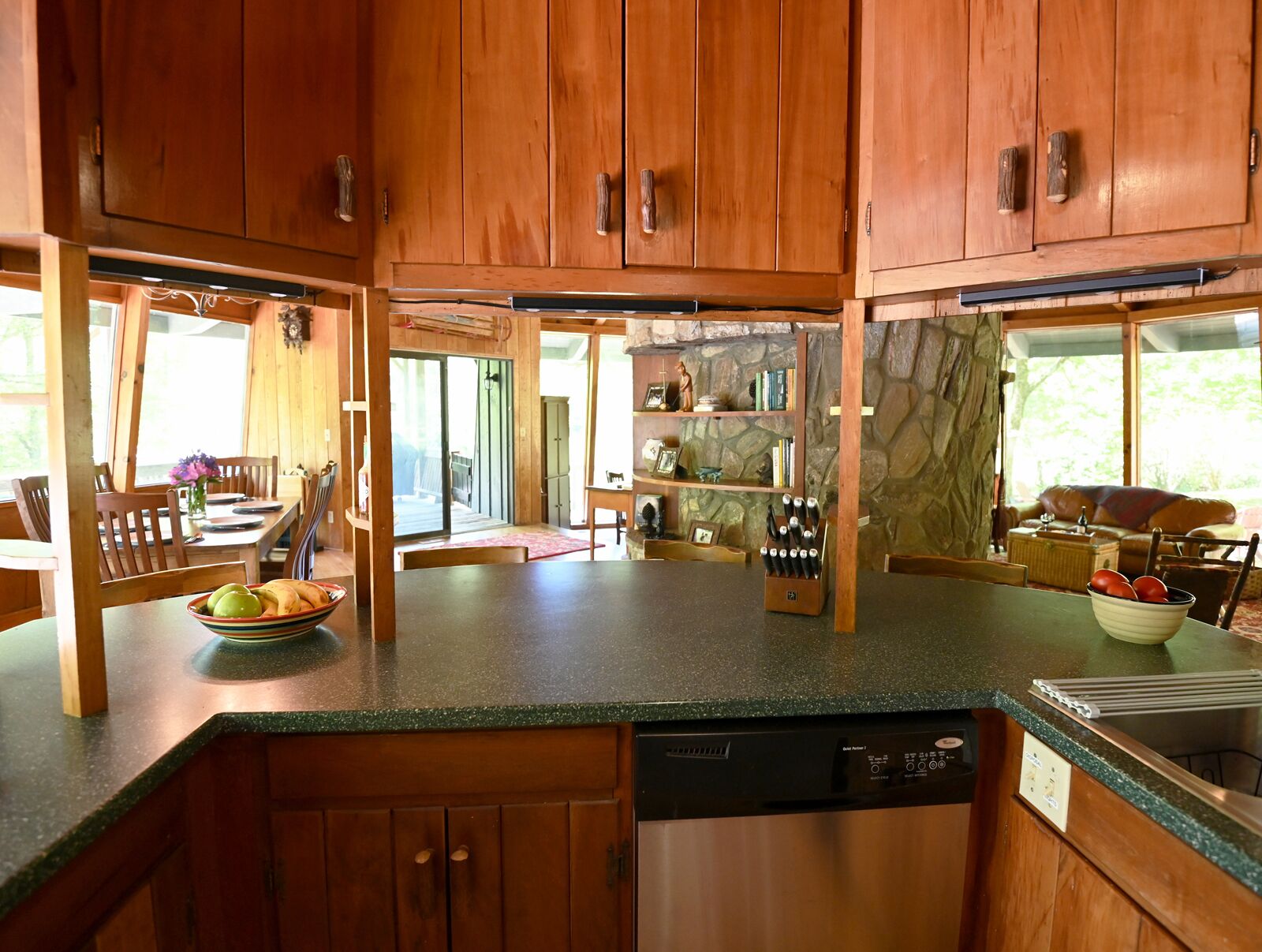 A kitchen with wooden cabinets, a dishwasher, and a stone wall.