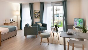 Moderni hotellihuone, jossa on sänky, kaksi nojatuolia, ruokapöytä tuoleineen, pieni sivupöytä ja televisio.