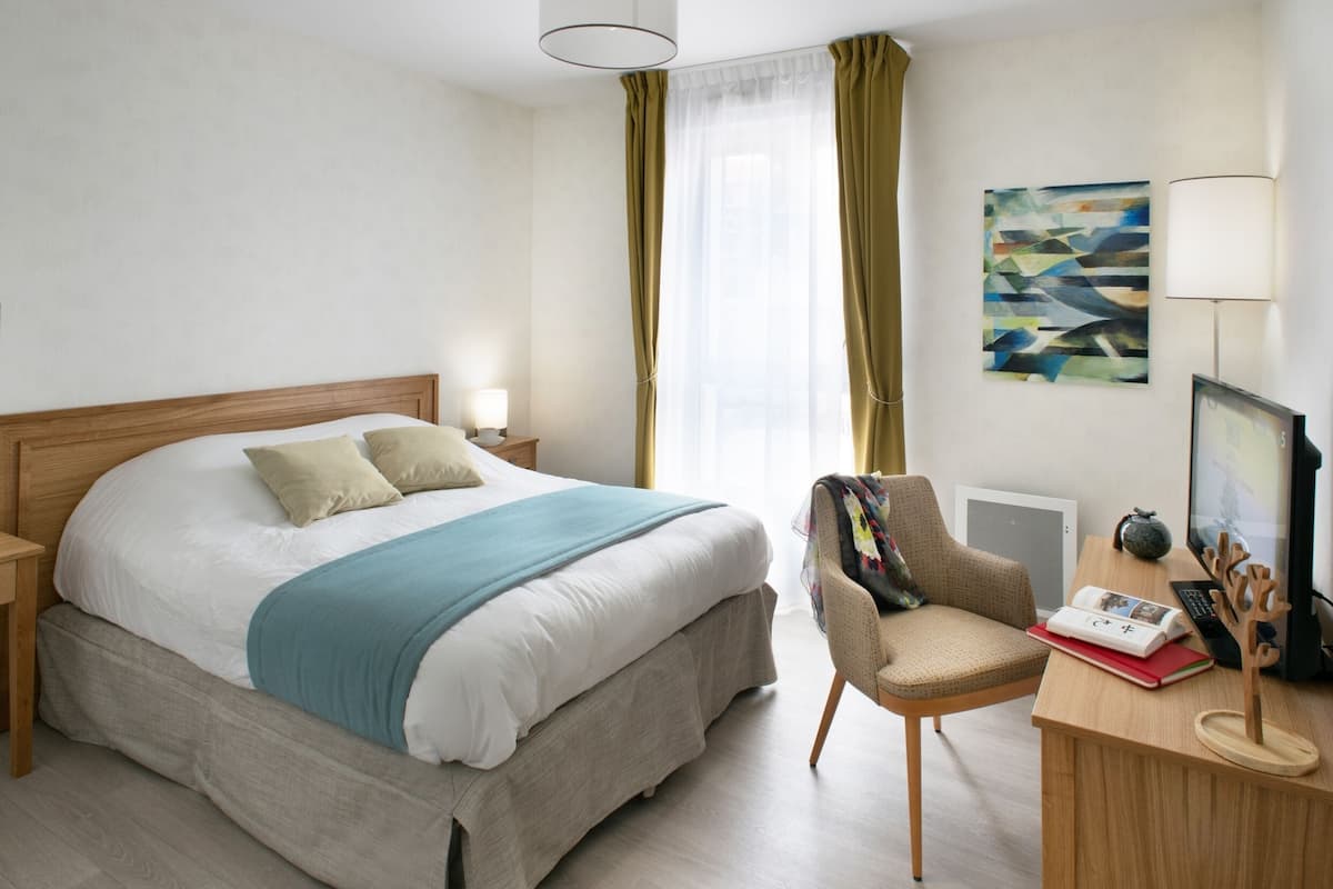 Ein modernes Hotelzimmer mit einem großen Bett, einem Schreibtisch mit Computer und einem Sessel.