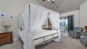 Ein Schlafzimmer mit Himmelbett, Nachttisch, Lampe, Stuhl und Blick ins Freie.