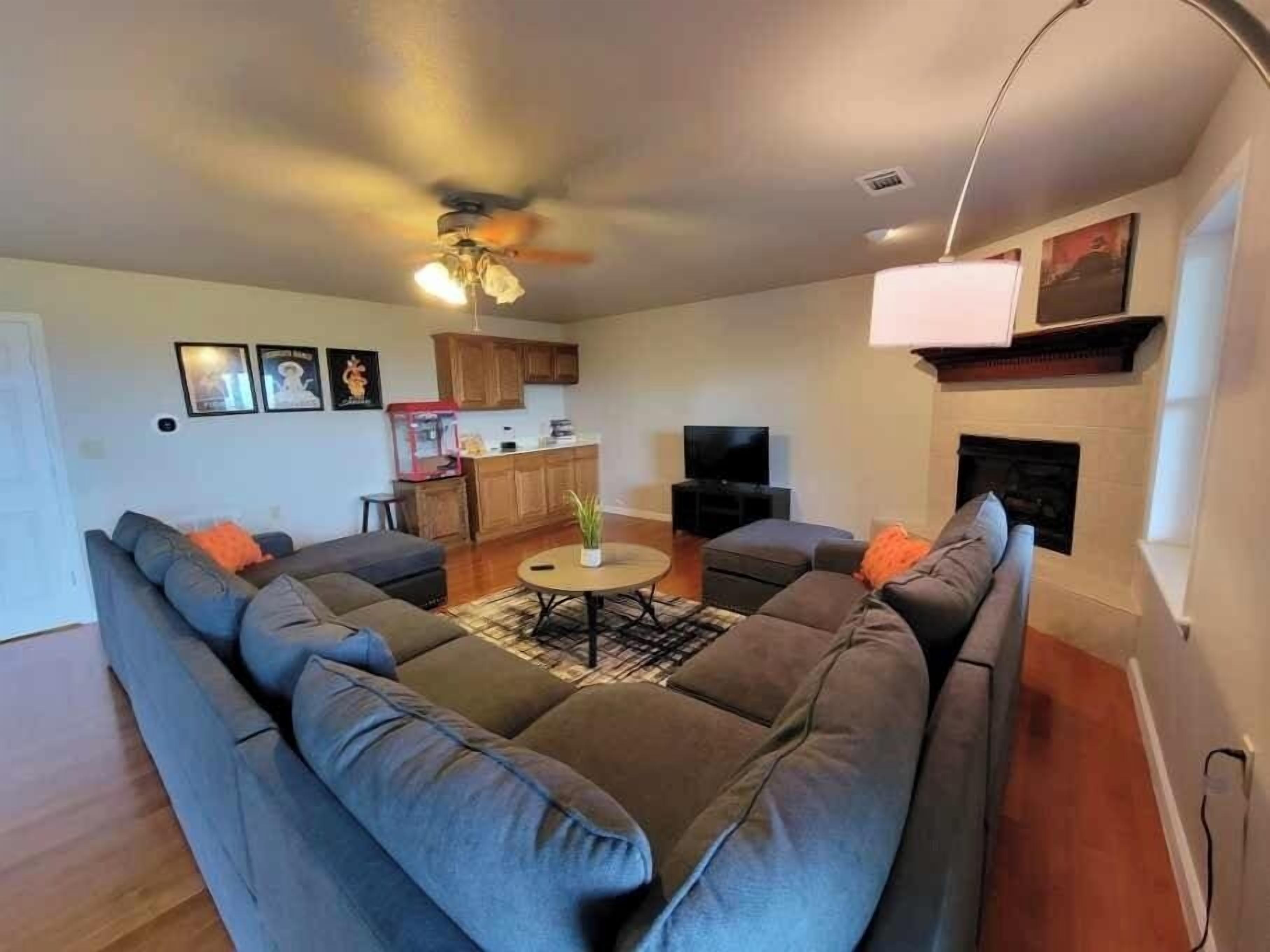 Uma sala de estar com sofá seccional, mesa de centro, ventilador de teto, televisão e lareira.