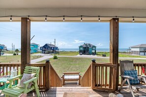 A wooden deck with a bench and chairs, overlooking a beach with houses and a clear sky. - CAMP QUEENIE - 2nd row with great views, steps to the surf and sand! (Crystal Beach)
